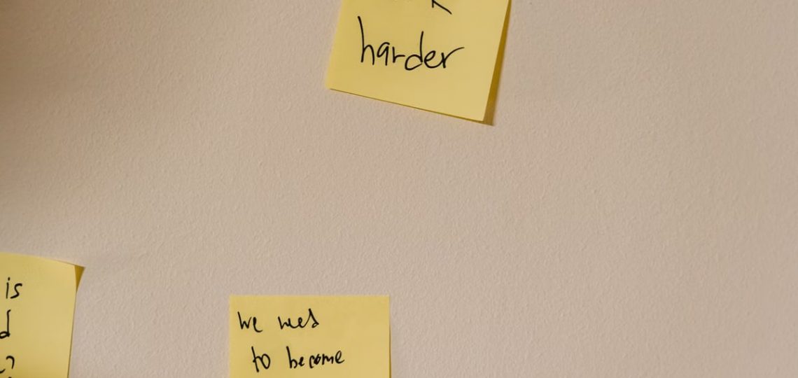Yellow sticky notes with motivational phrases posted on a white wall, inspiring action.